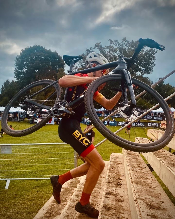 Photo of a racer carrying their bike up a set of wooden stairs with muddy footprints