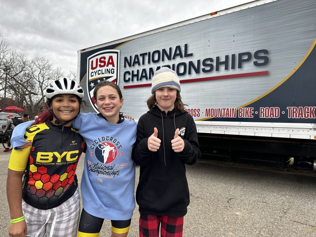 Photograph of three kids in front of a USA Cycling National Championships sign