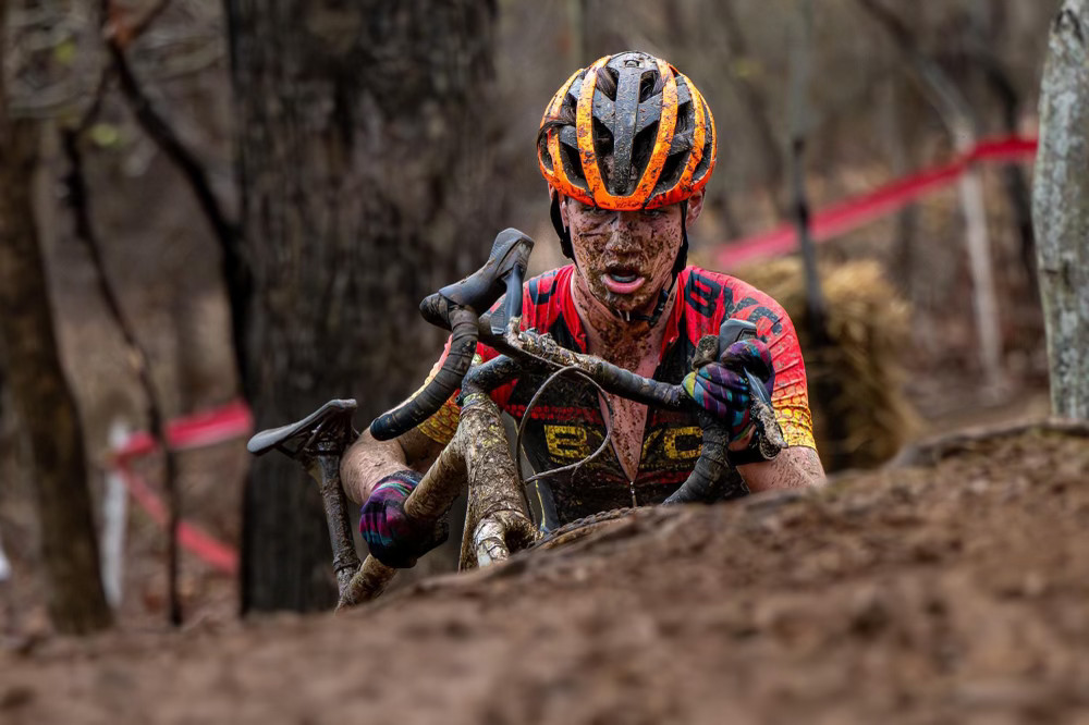 Photo of a racer covered in mud holding a bike